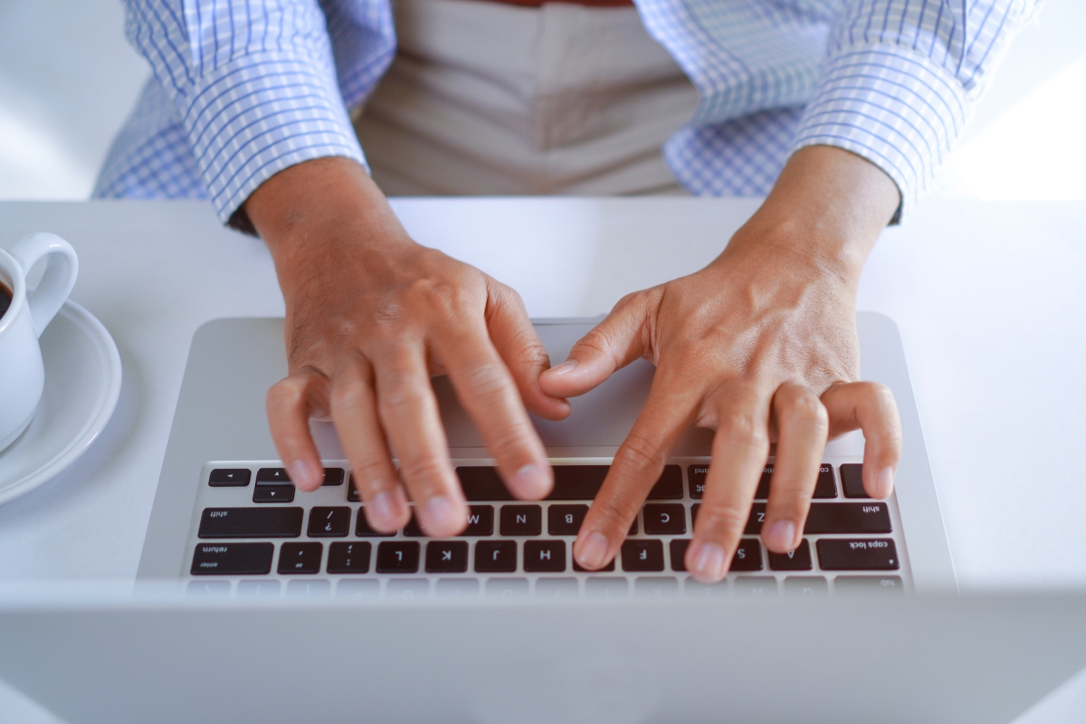 A person types on a laptop keyboard with both hands, perhaps searching for what is UX writing. A cup of coffee sits to the side.