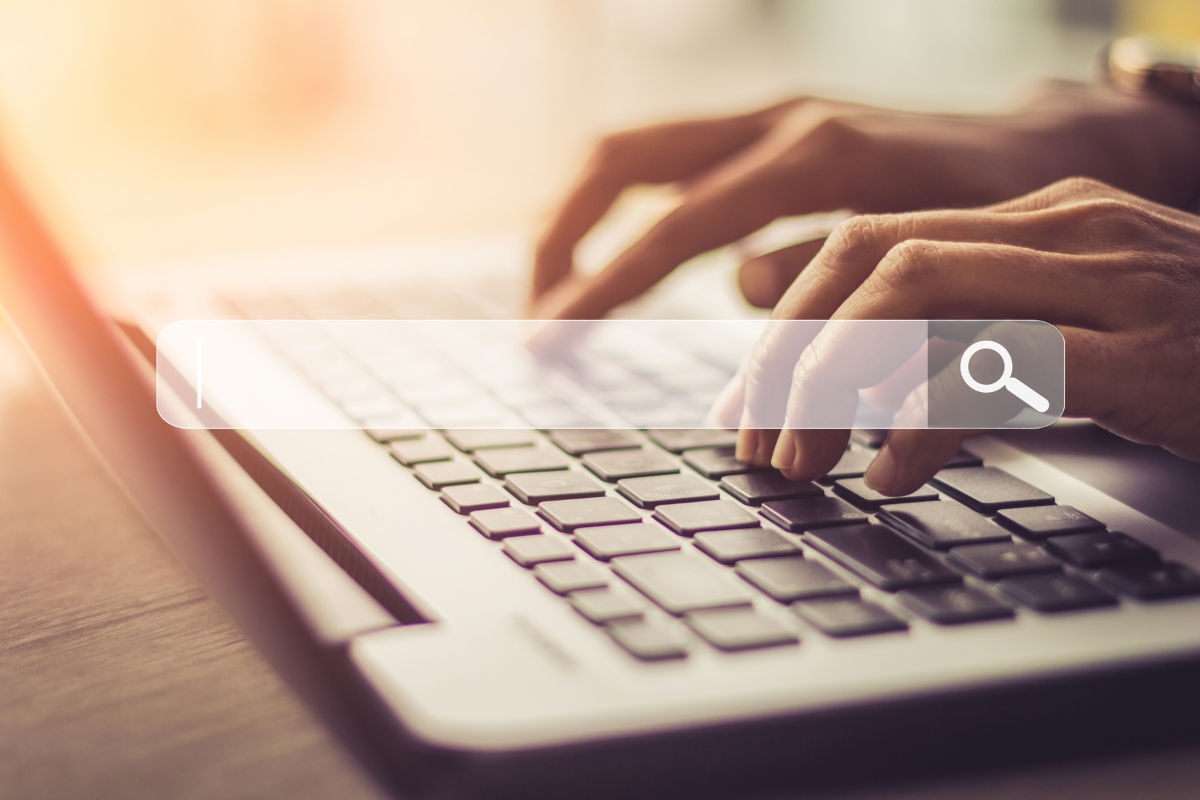 Close-up of hands typing on a laptop keyboard with a search bar overlay on the image, subtly hinting at the question "What is Ecosia search engine?