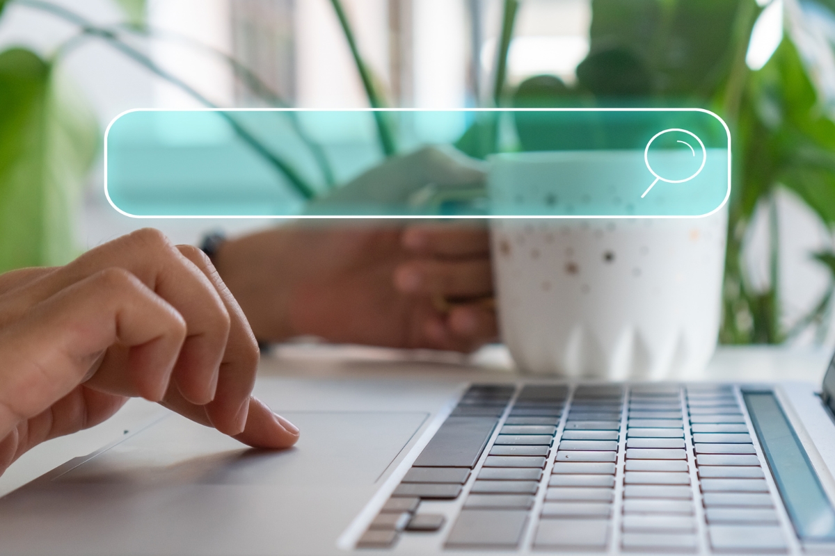 Close-up of hands on a laptop keyboard. One hand is using the touchpad, and the other is holding a white mug. A digital search bar icon with "what is Ecosia search engine" typed in is superimposed on the image.