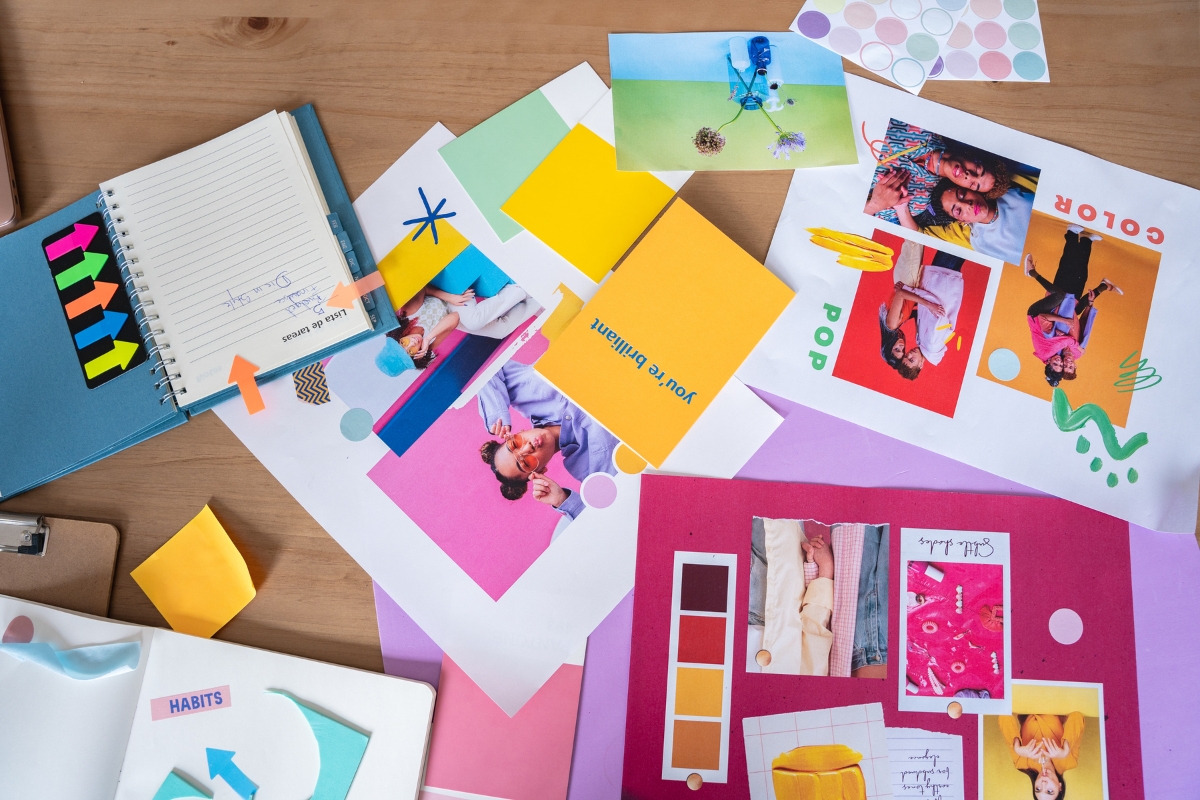 A cluttered desk with colorful mood boards, notebooks, sticky notes titled "What Is Hyperlocal Marketing," and various art supplies scattered around.