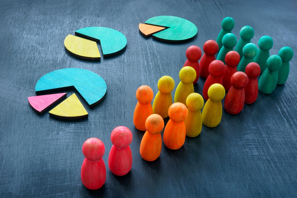         Colored wooden figurines grouped by color, standing next to pie charts with corresponding colors on a dark surface, illustrating data representation and demographics—highlighting *what is market segmentation* in a visual manner.