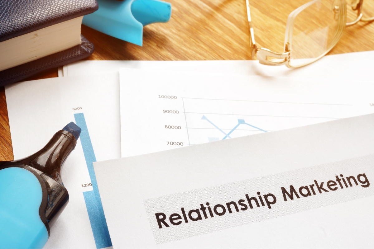 Close-up of a document titled "What Is Relationship Marketing" on a desk alongside a highlighter, a pair of reading glasses, and some charts.