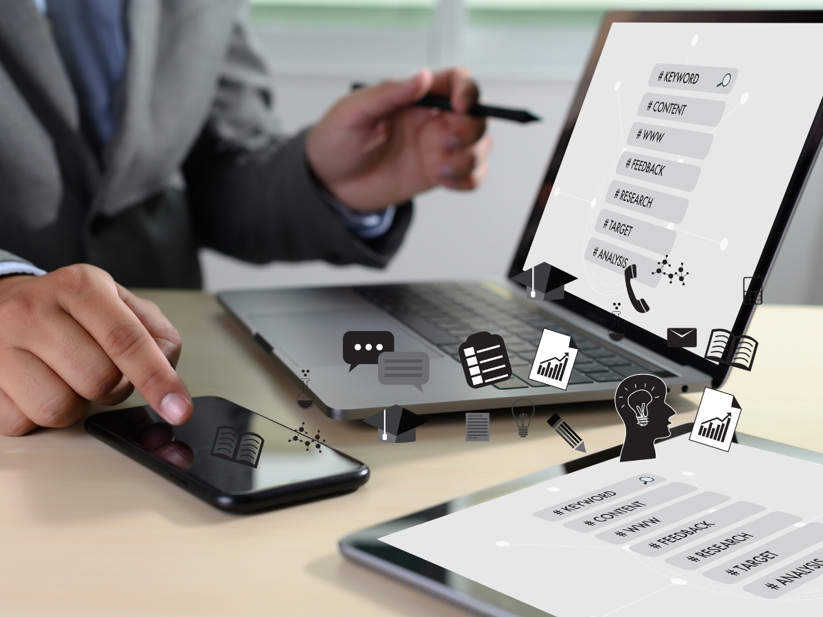 Person working at a desk with a laptop, smartphone, and overlay icons related to digital marketing and research, including charts, graphs, SEO symbols, and communication symbols.