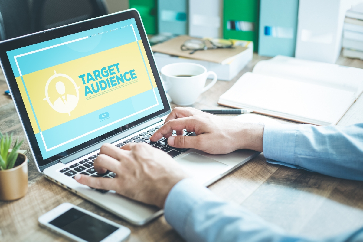 A person typing on a laptop displaying the text "Target Audience" on the screen, with a cup of coffee and office supplies on the desk, seamlessly integrating ai in marketing analytics.