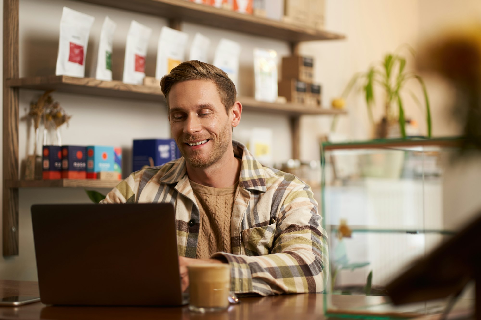 Portrait of cafe owner, young man sitting in coffee shop with laptop, working on data project