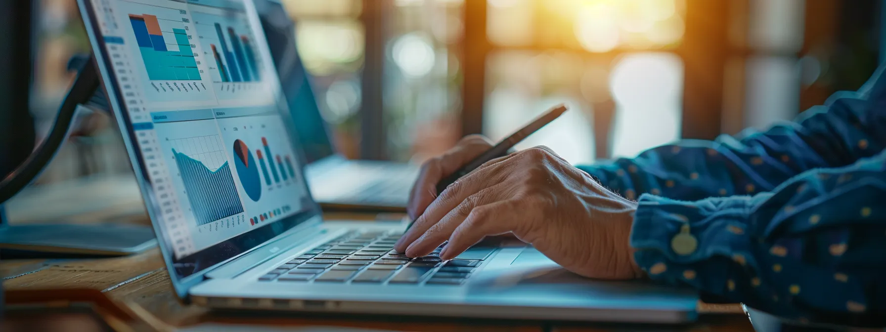 A person types on a laptop analyzing data charts displayed on the screen in a well-lit workspace.