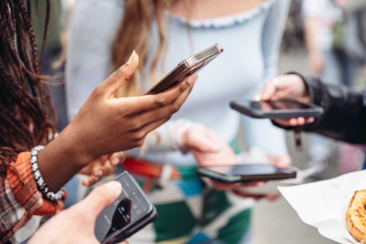 A group of people stand close together, all looking at their smartphones while holding them in their hands, perhaps searching for how to come up with content ideas.