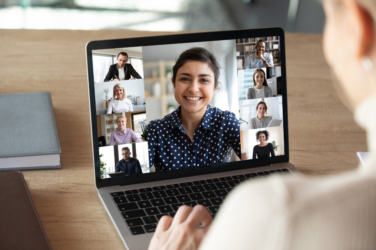 A person participates in a video conference call on a laptop screen, with eight other people in individual windows discussing how to come up with content ideas, all engaging actively in the virtual meeting.