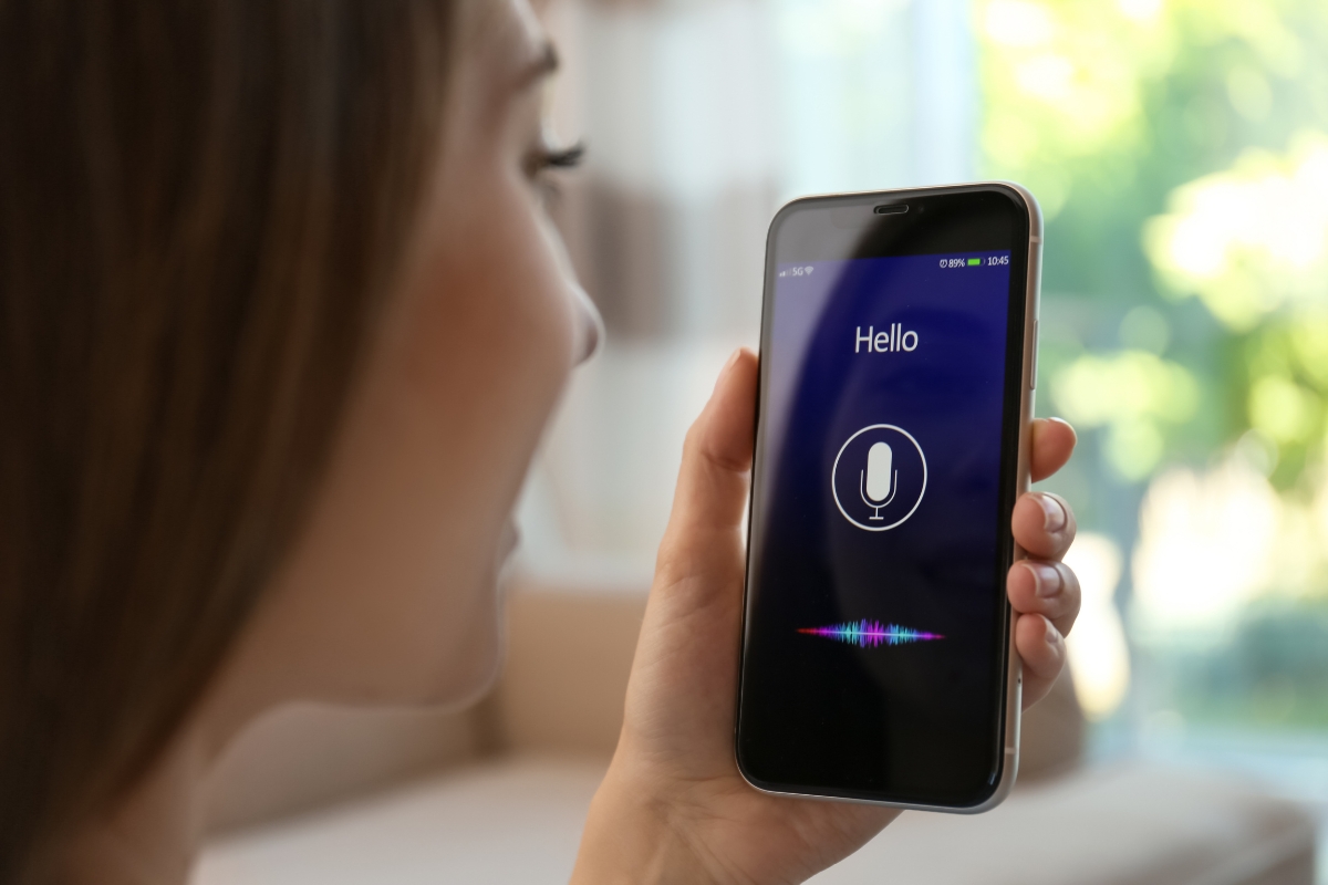 A person holds a smartphone displaying a voice assistant app with the text "Hello" and a microphone icon on the screen, highlighting how to optimize your website for voice search in the digital age.