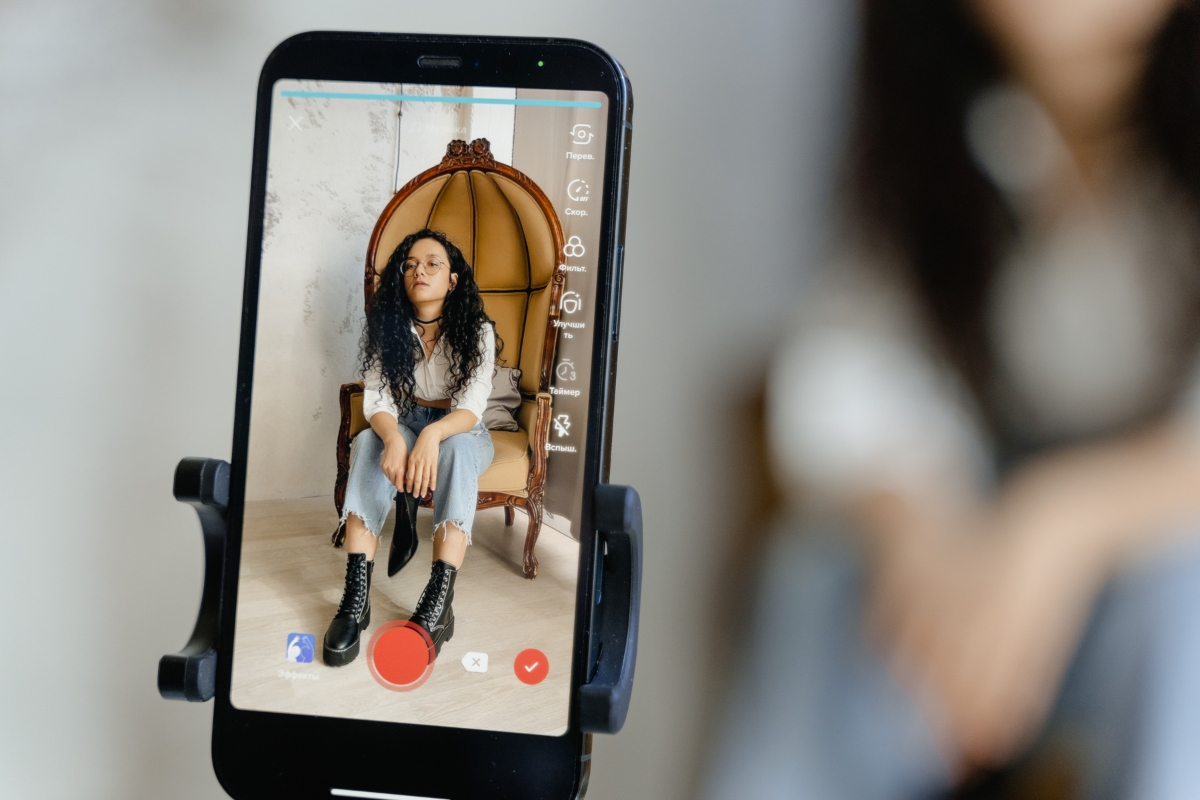 A person with long curly hair sits on a chair inside a room, captured through a smartphone camera screen, ready for recording or live streaming—a perfect moment to discuss influencer marketing ROI for small businesses.