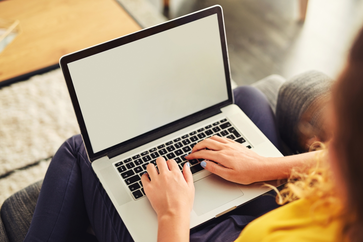 A person types on a laptop with a blank screen while sitting on a couch, brainstorming LinkedIn Marketing Tips.