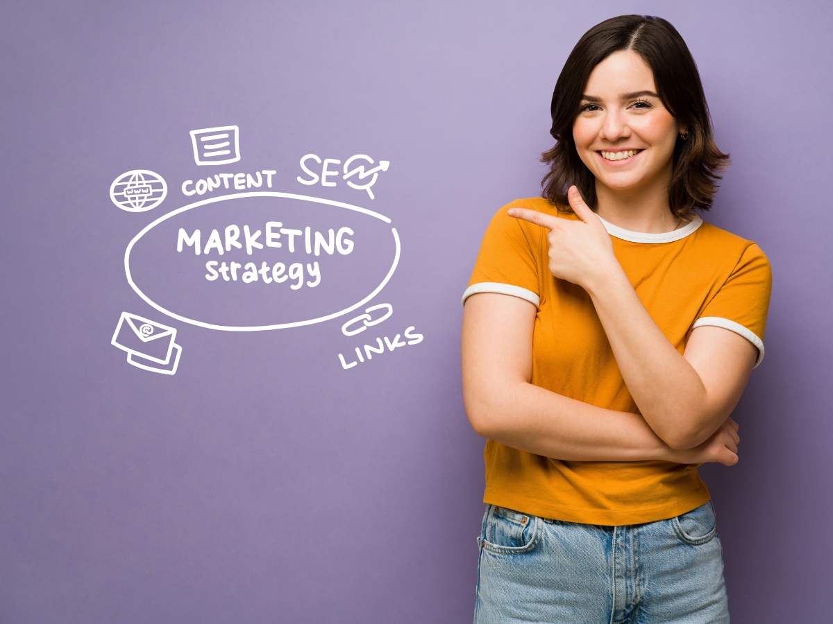 Smiling person in a yellow shirt pointing to a marketing strategy diagram on a purple wall. The diagram includes words like content, SEO, links, and local content marketing.