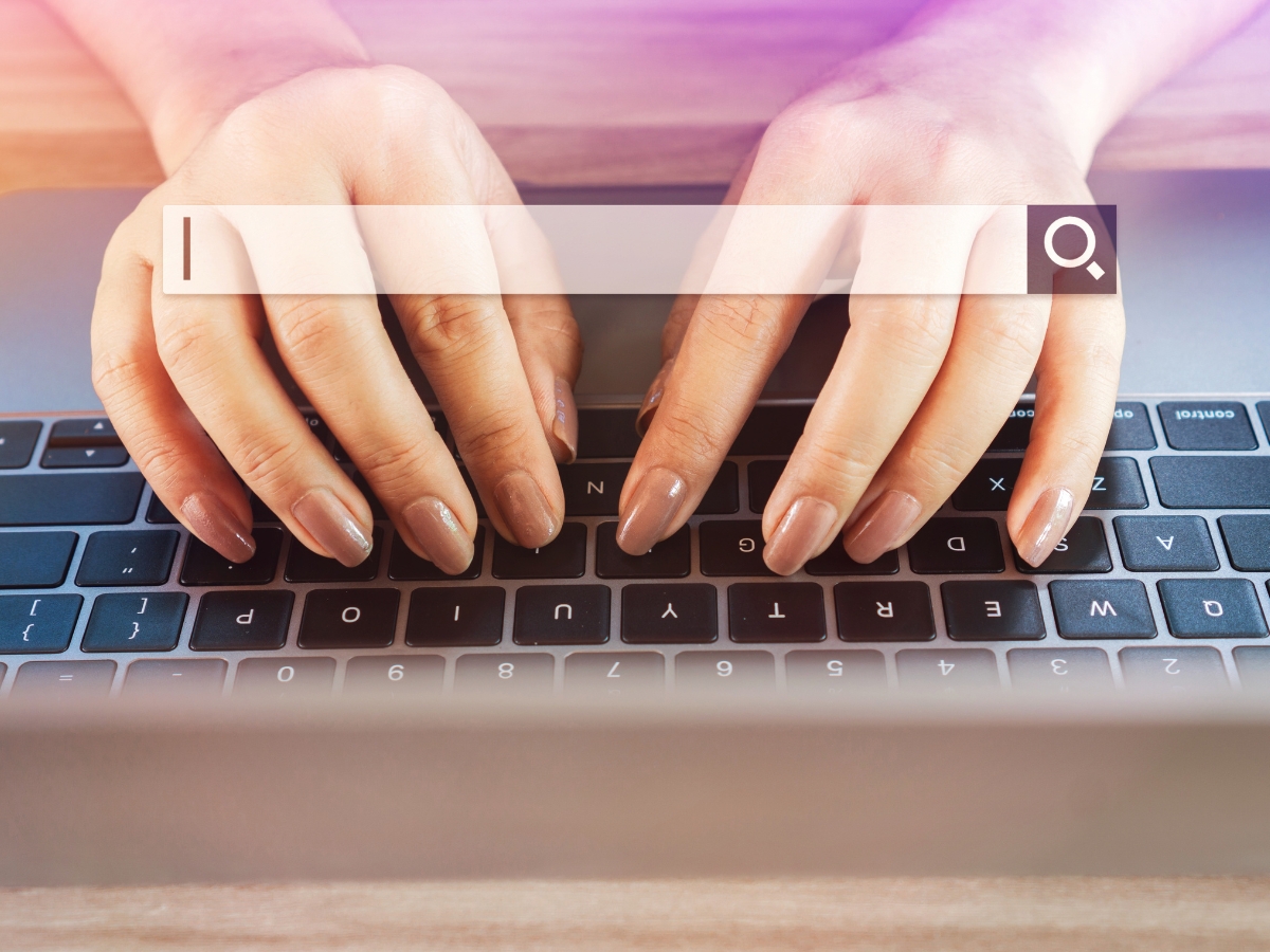 Close-up of a person's hands typing on a laptop keyboard, with a search bar graphic overlay at the top of the image displaying low competition keywords.