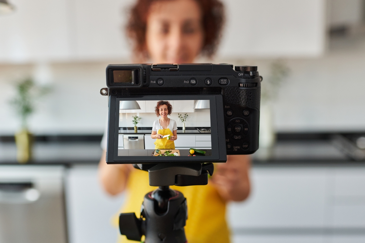 A person wearing a yellow apron is being filmed while cooking in a modern kitchen, perfect for marketing with Instagram Reels. The camera screen shows their image in focus.