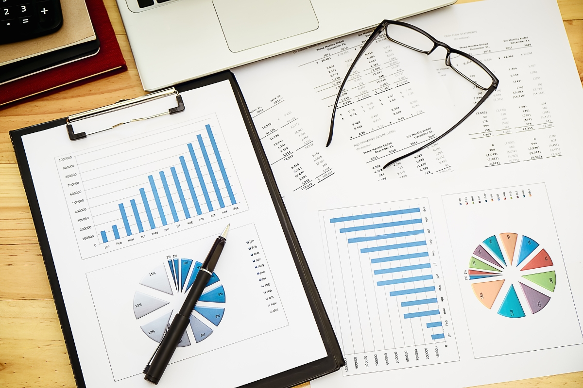 A desk with financial charts, graphs, a pen, glasses, and a laptop. The charts include bar graphs and pie charts on sheets of paper, highlighting strategies for niche marketing.