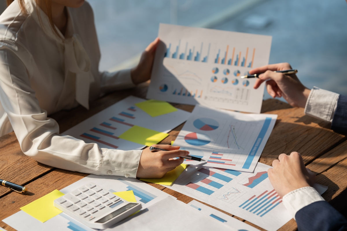 Two people analyzing financial graphs and charts on a wooden table, discussing strategies for niche marketing, with a calculator and sticky notes nearby.