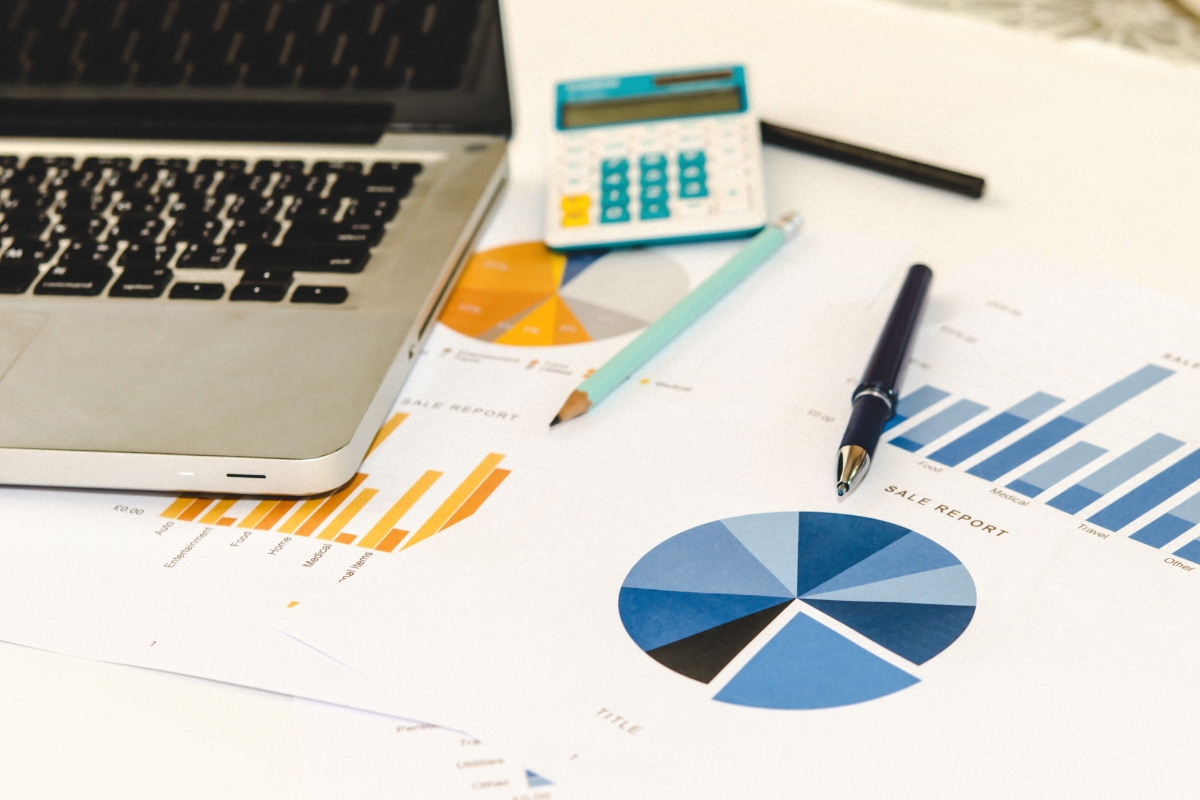 A workspace with a laptop, calculator, pen, pencil, and financial reports featuring pie and bar charts on a desk highlights the critical role of niche marketing in driving targeted business insights.