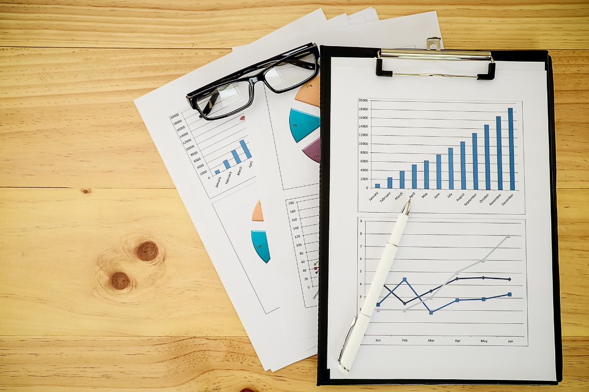 A clipboard with financial charts and graphs, a pen, and a pair of glasses on a wooden desk reflects the precision needed for real-time marketing analysis.