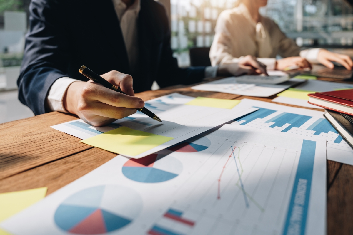 People working at a desk analyzing graphs and charts with documents and sticky notes spread out, all essential for real-time marketing.