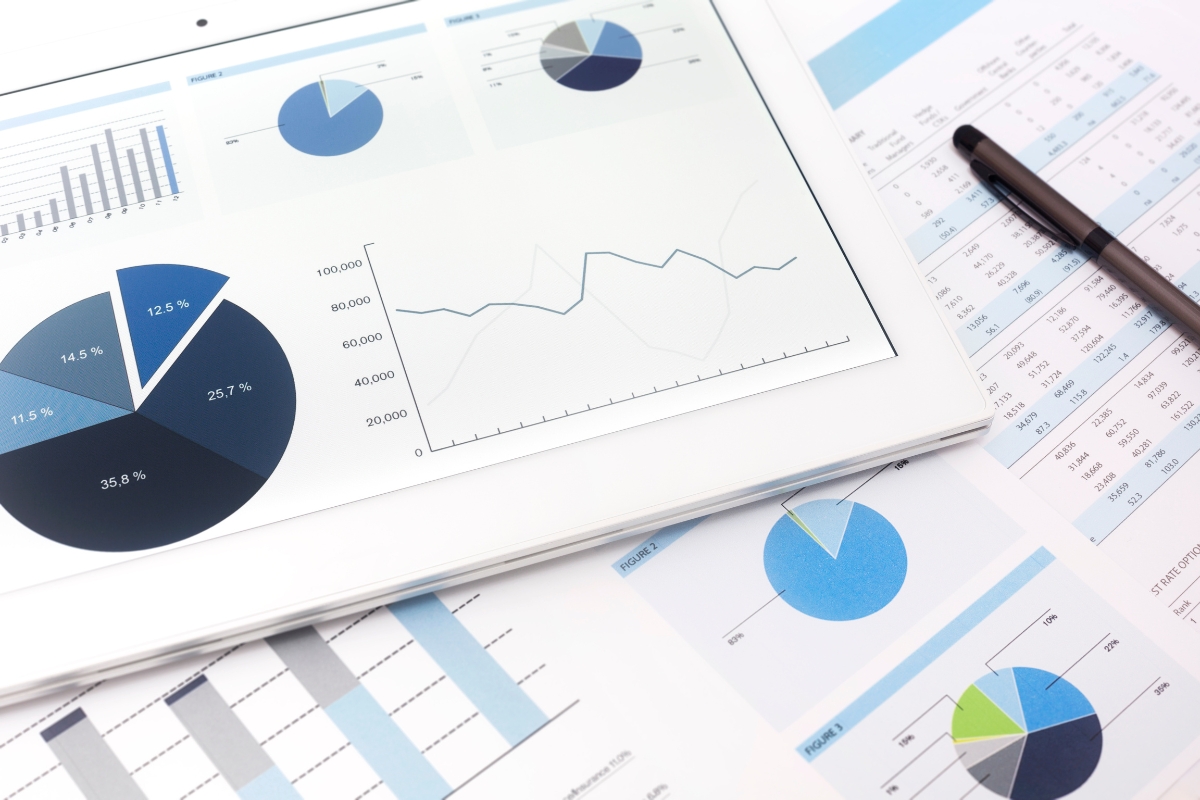 A tablet displaying various charts and graphs, surrounded by printed documents and a pen, depicting financial or statistical data analysis for real-time marketing strategies.