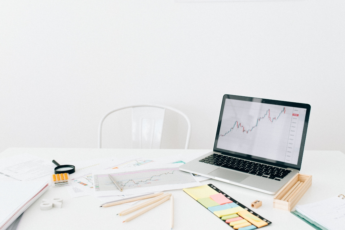 A cluttered desk with a laptop showing a rising graph, papers, pencils, a calculator, a magnifying glass, sticky notes, and drawing tools scattered around—perfect for brainstorming retargeting vs remarketing strategies.