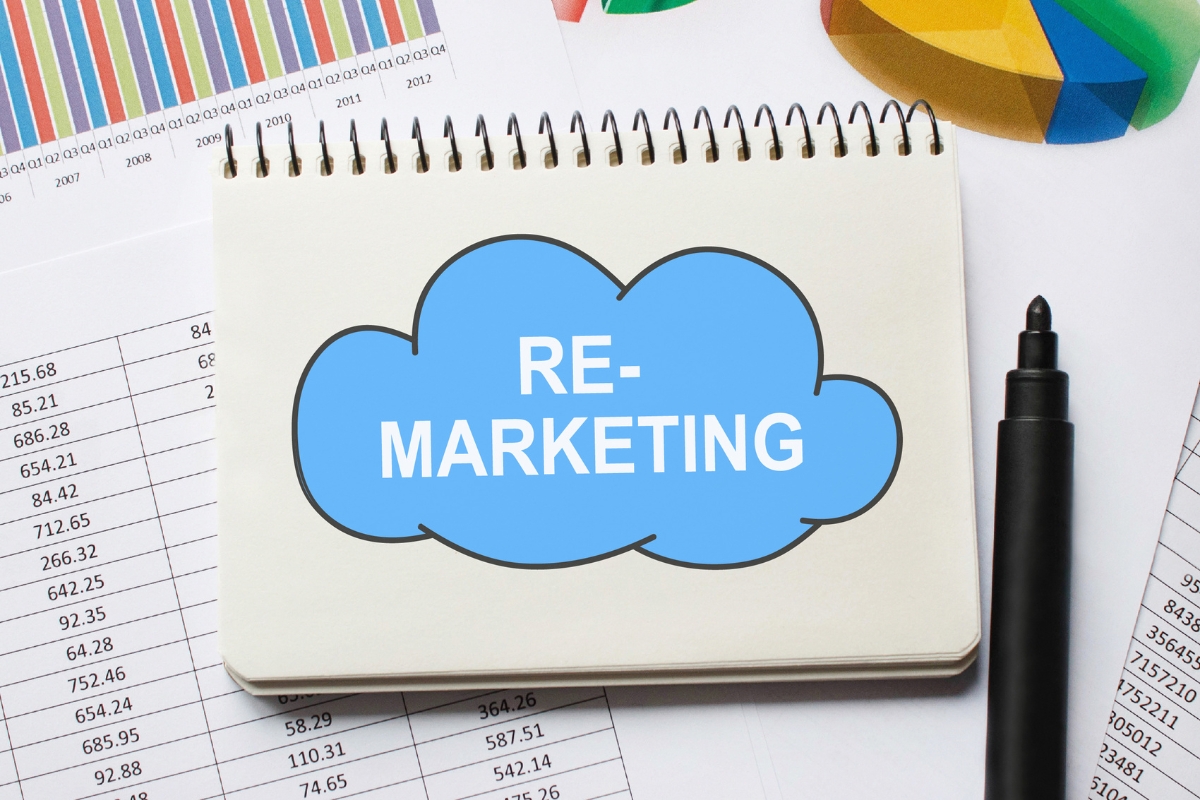 A notebook displaying the phrase "What Is Remarketing" in a blue cloud shape, placed on top of documents with charts and graphs. A black pen is situated to the right of the notebook.