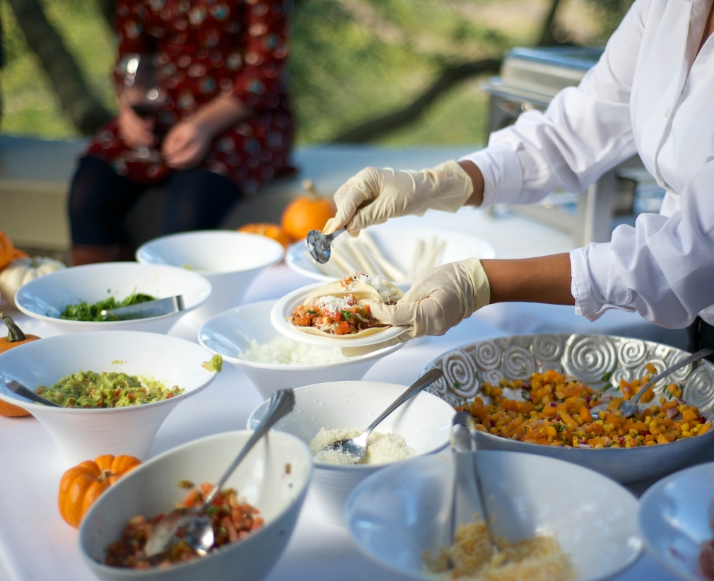 Caterer in gloves serving food from a buffet table with various dishes and small pumpkins schedule using a catering crm platform.