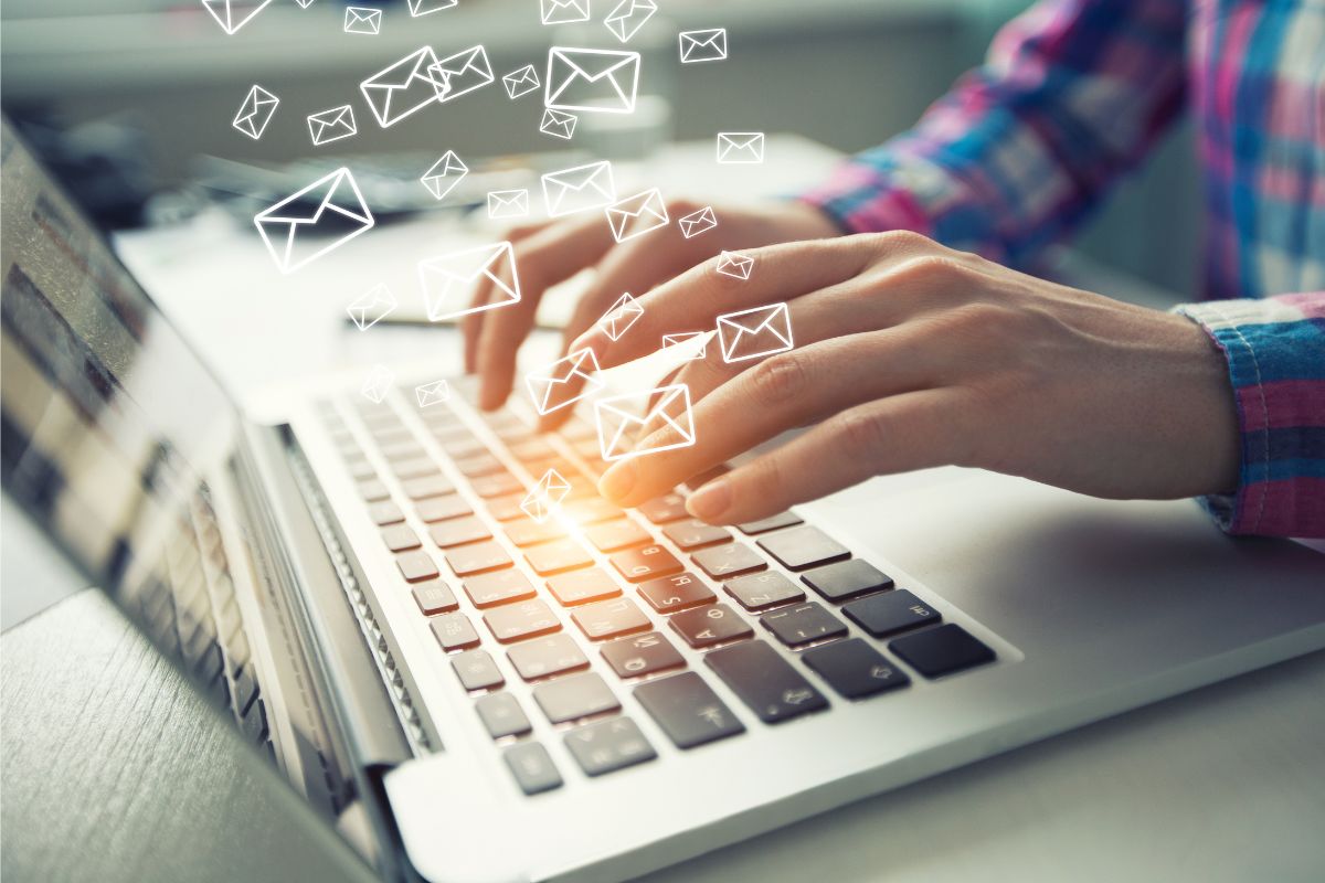 A person is typing on a laptop keyboard with illustrated email icons hovering above, representing email marketing automation tools and the seamless sending of emails.