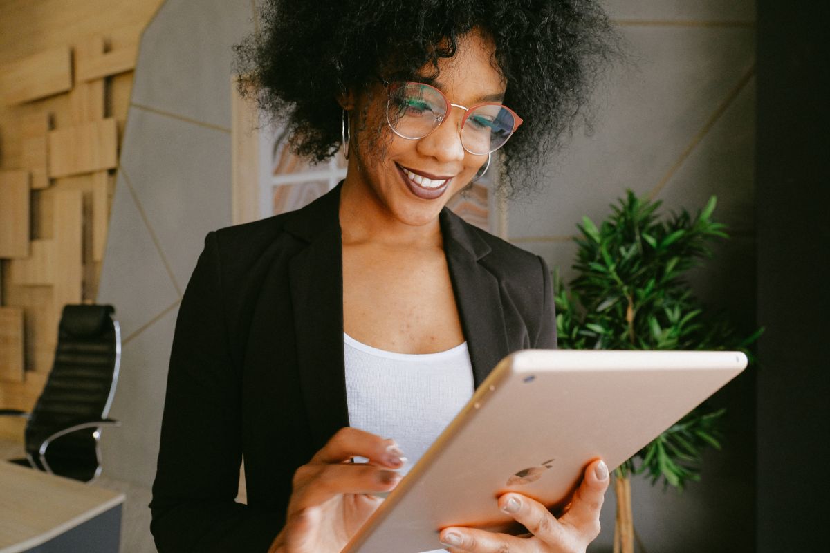 A person in a blazer and glasses is smiling and using a tablet in an office setting with a chair, plant, and CRM integration tools in the background.