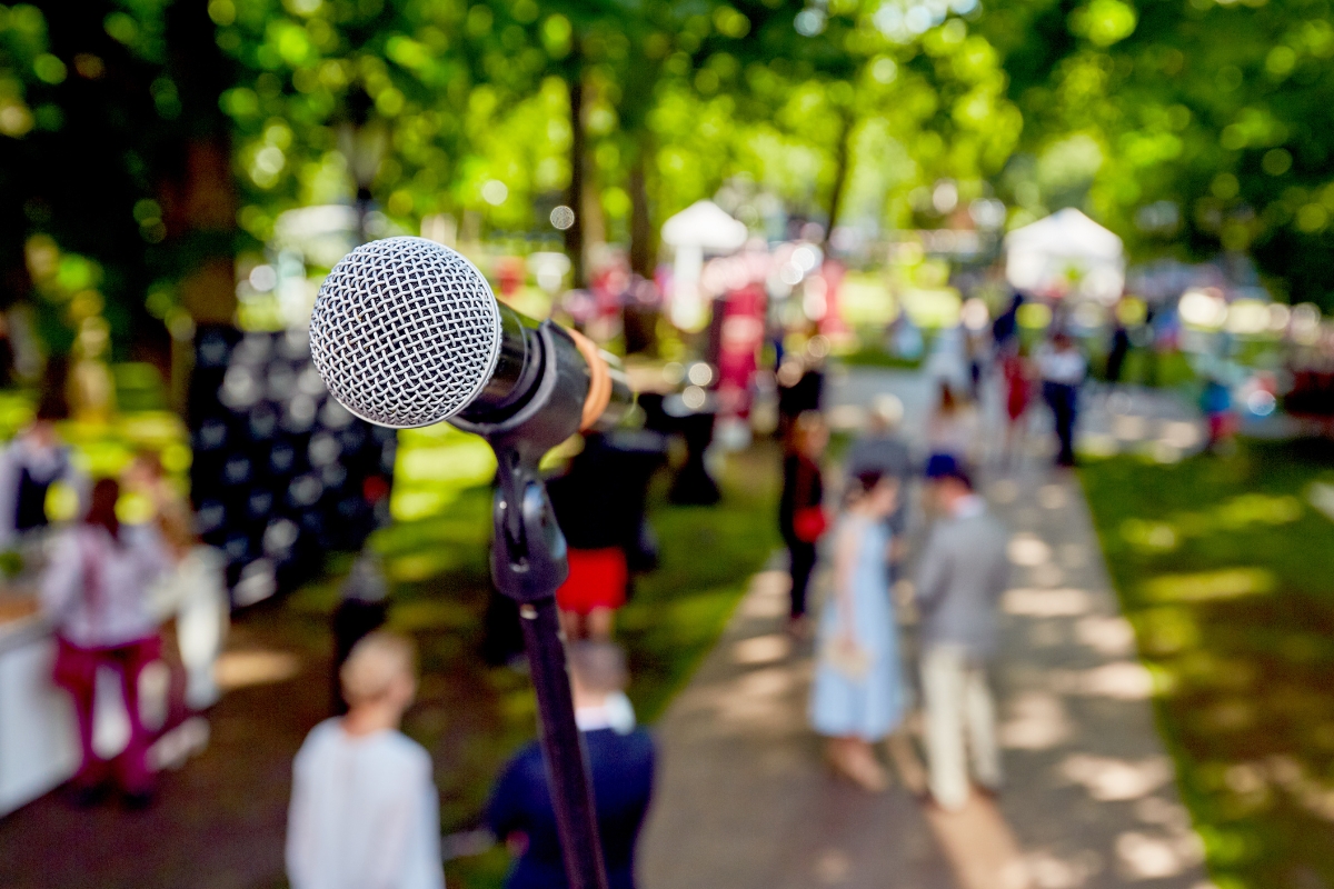 Close-up of a microphone on a stand set up in an outdoor area with blurred people and tents in the background, creating the perfect setting to share tips on how to market your small business.