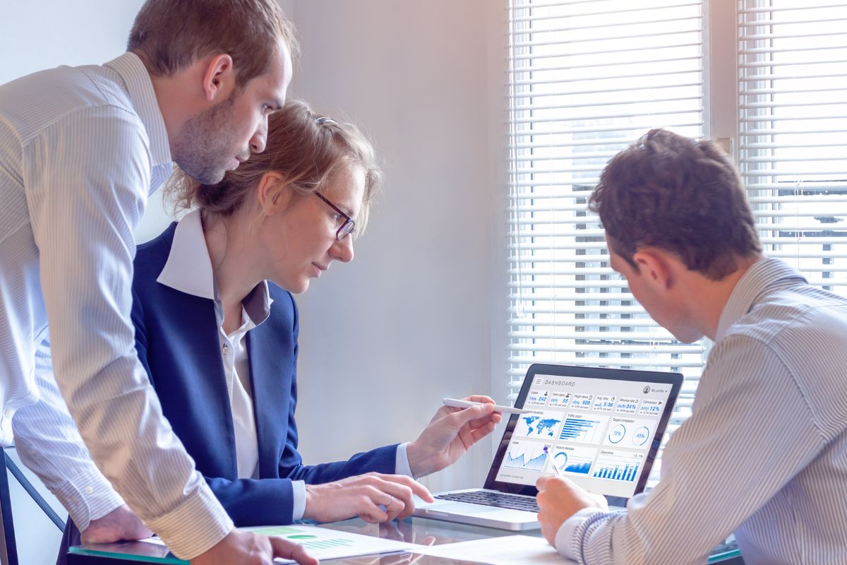 Three business professionals reviewing graphs and charts on a laptop at a table in a well-lit office, analyzing CRM data to optimize their marketing automation strategies.