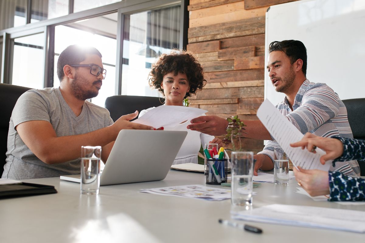 Four people are seated around a table in a modern office, collaboratively reviewing documents to ensure there is no duplicate content in SEO reports.