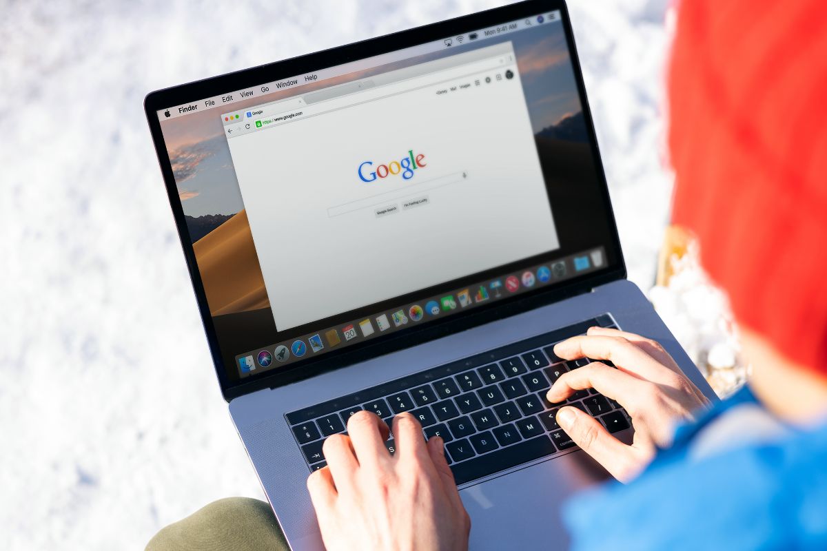 A person is using a MacBook laptop, browsing the Google search page, while sitting in a snowy outdoor setting, perhaps researching robots.txt for SEO.