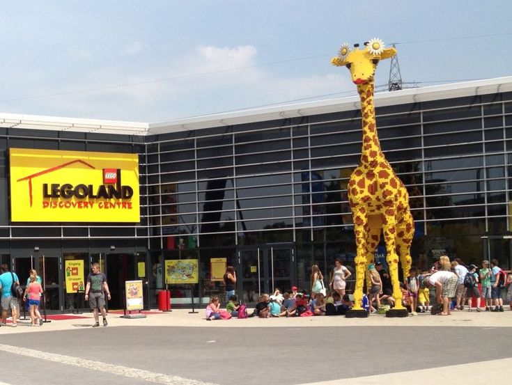 Entrance of Legoland Discovery Center Atlanta featuring a large LEGO giraffe statue and people gathering outside.