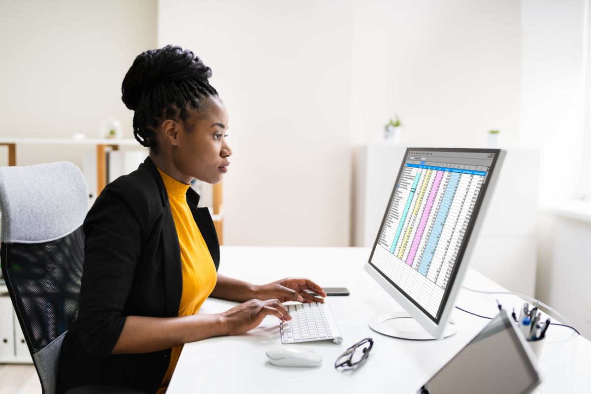 A woman in an office sits at a desk, working on a desktop computer displaying an automated spreadsheet, showcasing the power of affordable automation.