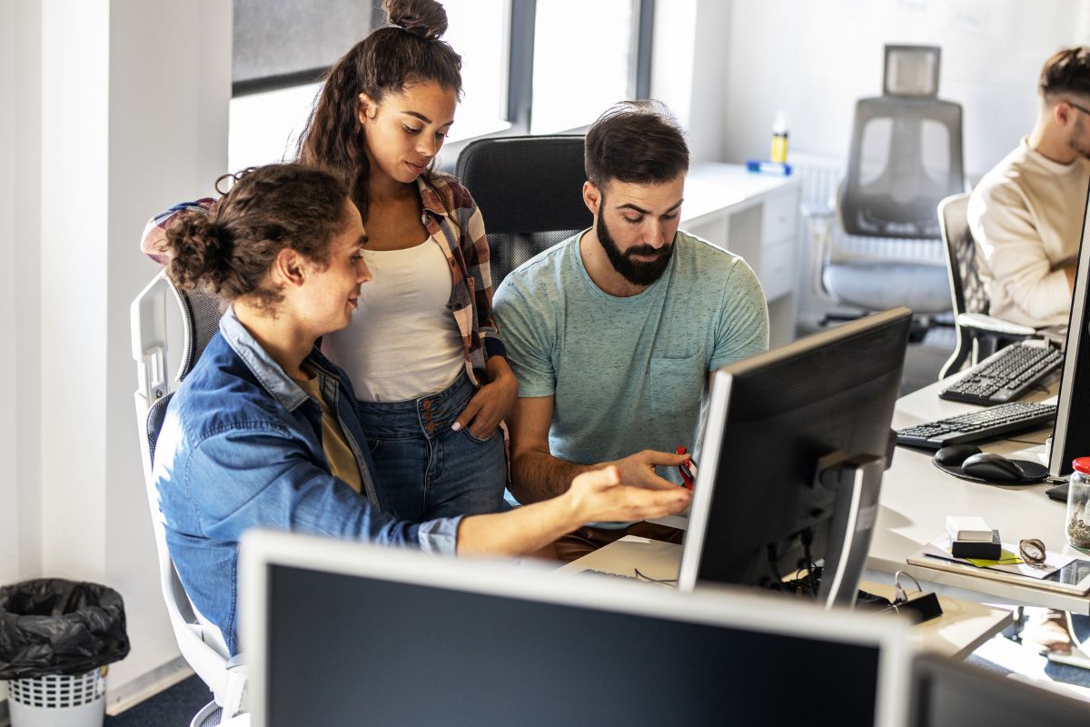 Three people collaborating at a computer desk in an office, discussing affordable automation solutions displayed on the screen.