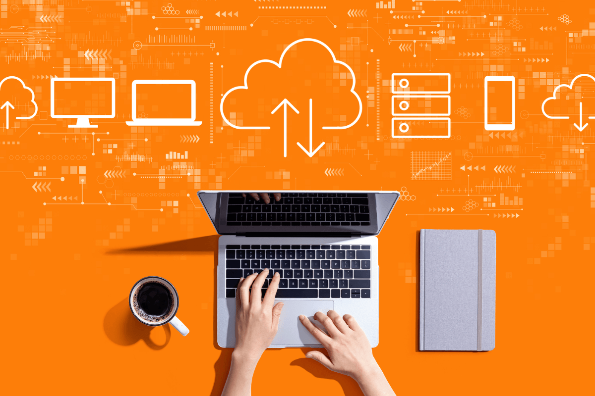 Hands typing on a laptop, with cloud icons, servers, and various device illustrations above, symbolizing cloud computing and data synchronization, on an orange background. A coffee and notebook are beside the laptop, ideal for setting up the best WordPress backup solutions.