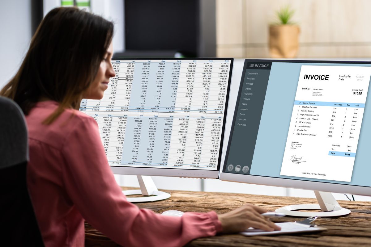 A woman in a pink blouse works at a desk with two monitors; one displaying a spreadsheet and the other an invoice, highlighting her seamless workflow automation. A potted plant and office supplies are visible in the background.