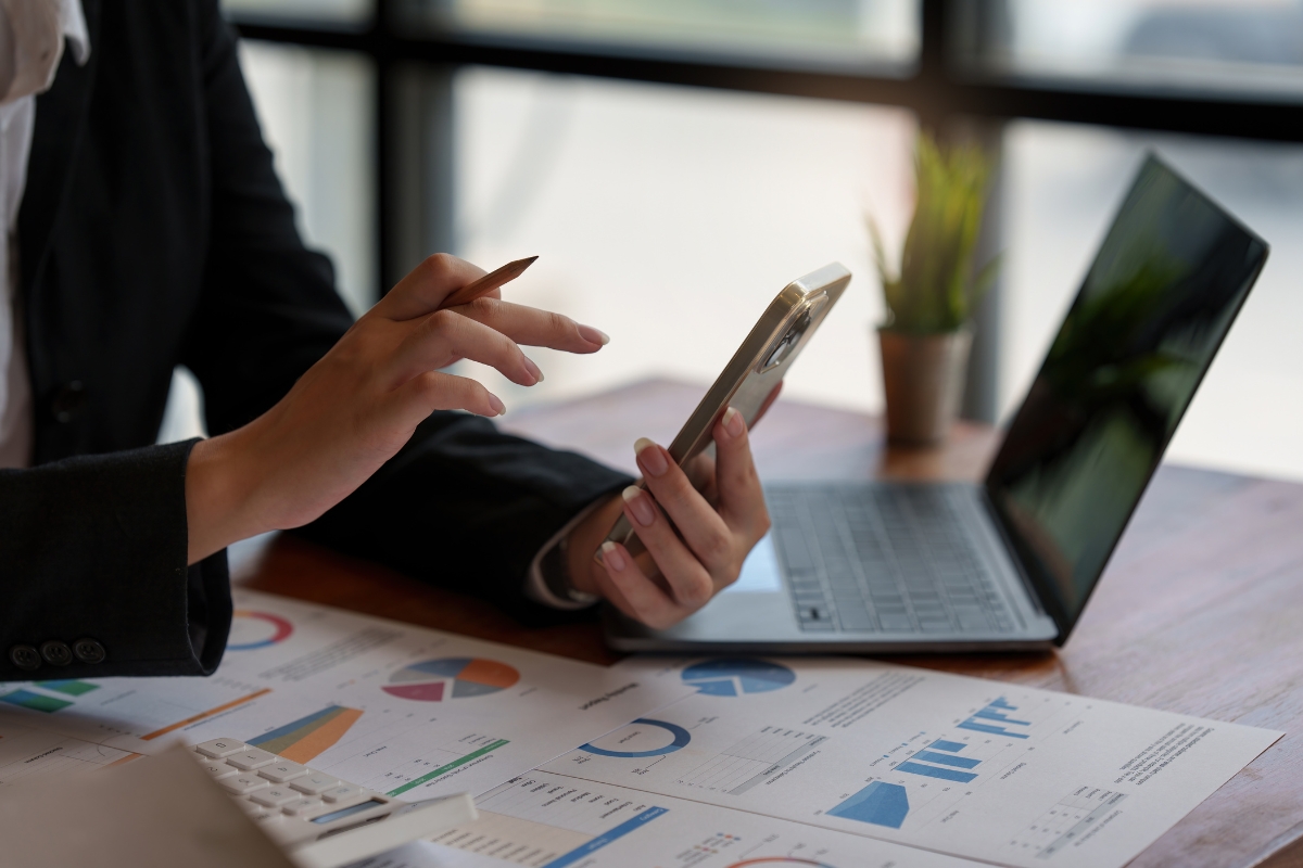 A person engaged in conscious marketing, using a smartphone with charts, graphs, and a laptop on a desk.