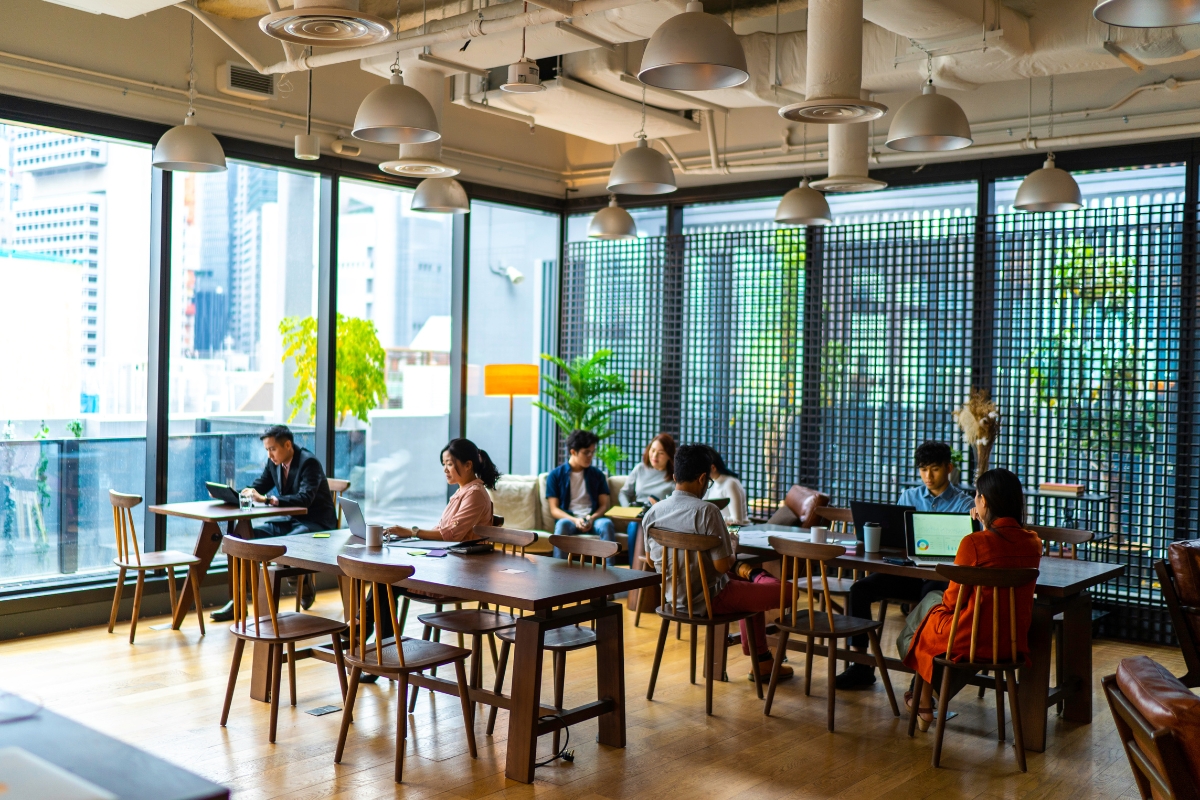 People working and collaborating in a modern office space with large windows, wooden tables, and indoor plants, typical of the coworking spaces in Marietta.