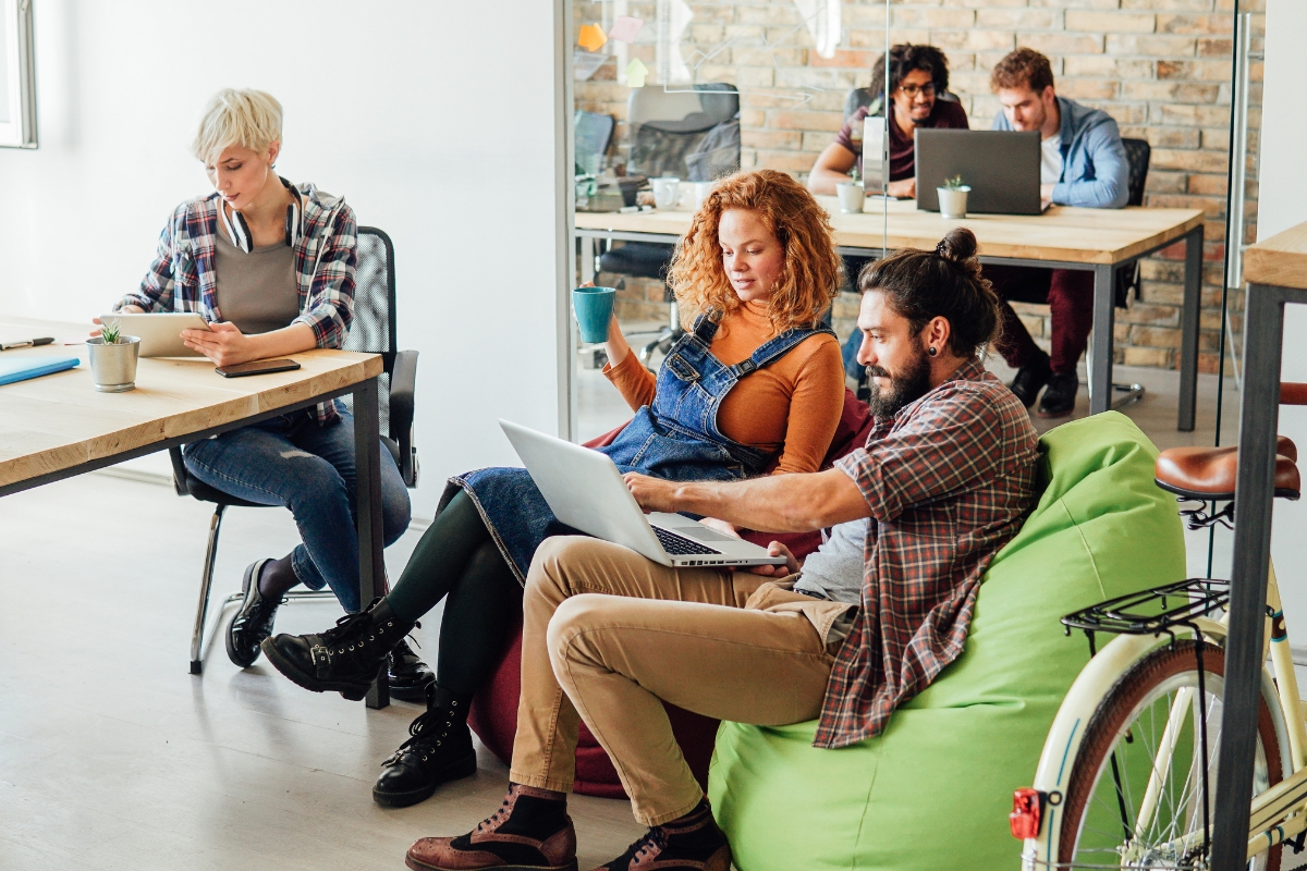 Several people are working on laptops and notebooks in an open office space. Two individuals, seated on a green bean bag chair, are discussing something on a laptop screen. This snapshot perfectly captures the collaborative vibe of coworking spaces in Marietta.