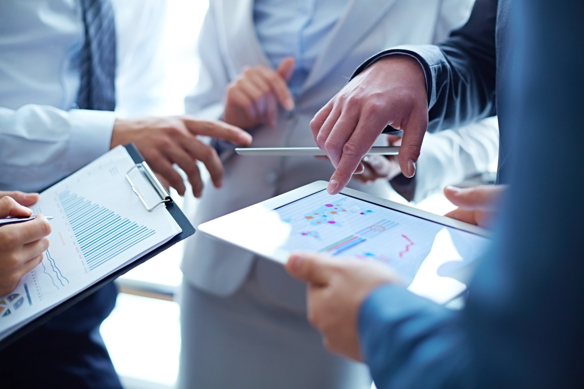 Business professionals discussing customer data management and best CRM practices, along with data and charts on tablets and documents in a meeting.