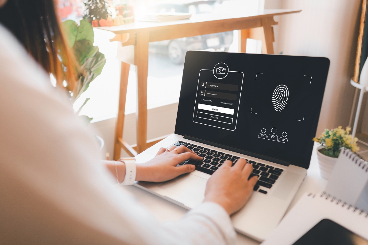 Person using a laptop with a login screen displayed, showing username and password fields, and a fingerprint icon for biometric authentication. The setting appears to be a well-lit office space, ideal for implementing CRM best practices or managing sensitive customer data efficiently.