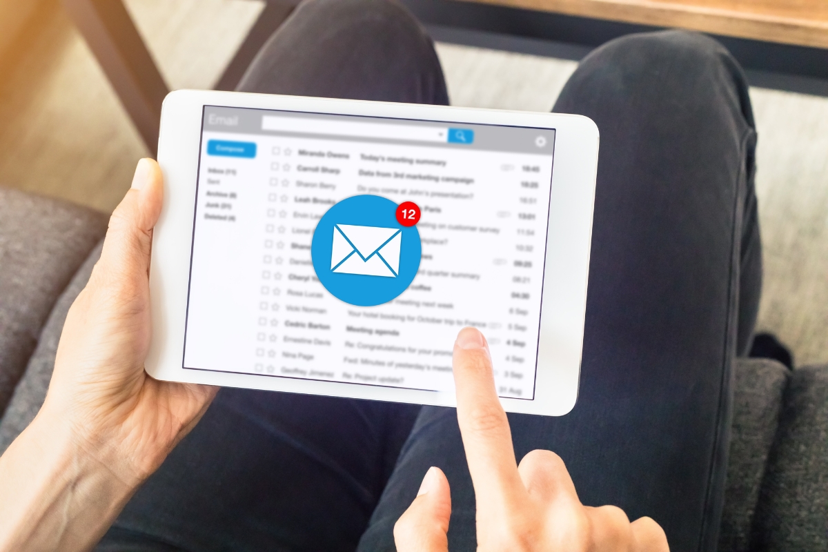 A person is using a tablet to check email, discovering 12 new messages. Among these, several highlight the importance of effective email signature marketing for boosting professional communication.