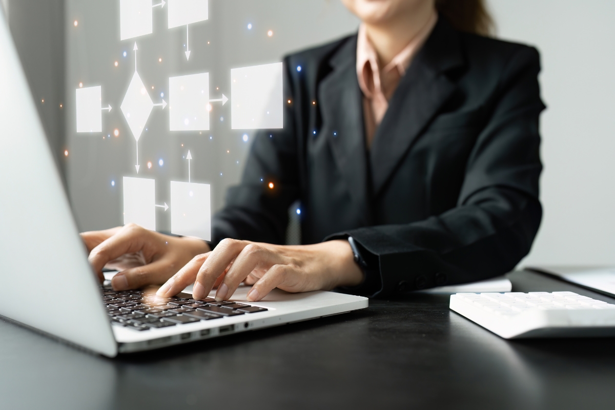 Person in a suit working on a laptop with floating digital flowchart icons above the keyboard, focusing intently on sales pipeline management.