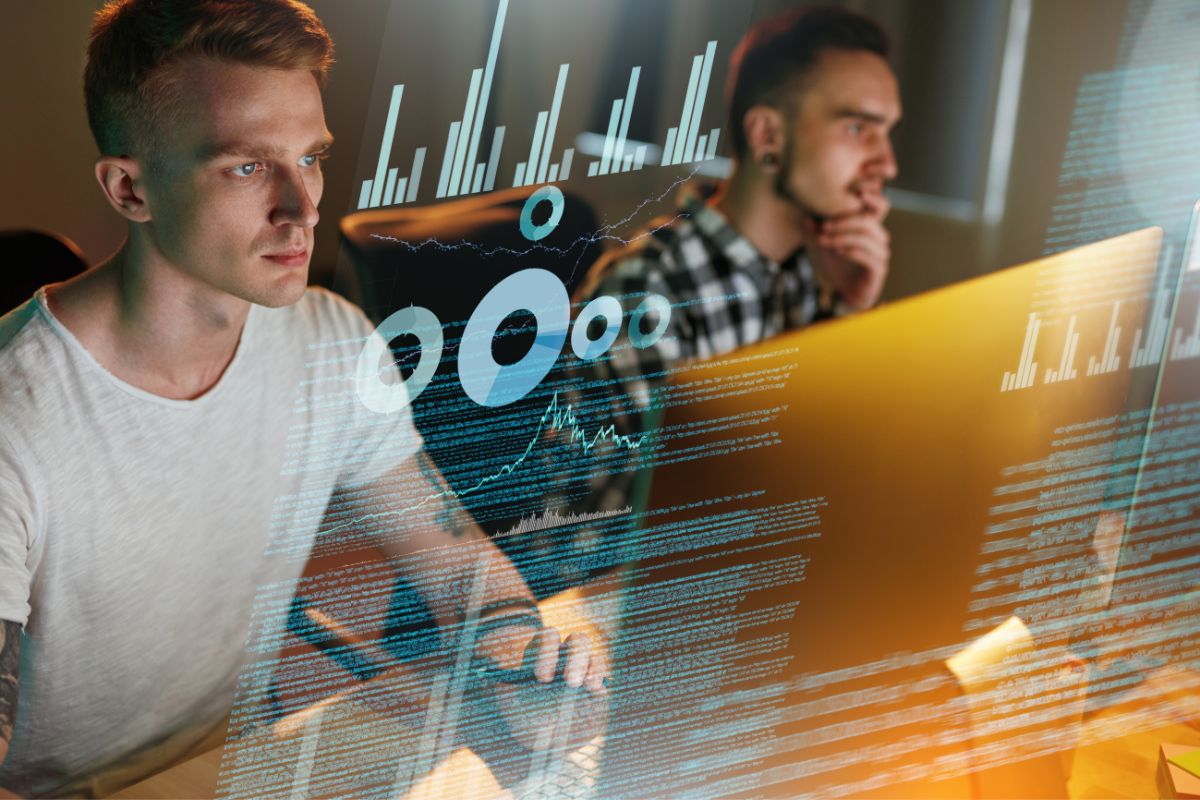 Two men are working on computers with graphs and data projections overlaying in the foreground, seamlessly integrating workflow automation to enhance productivity.