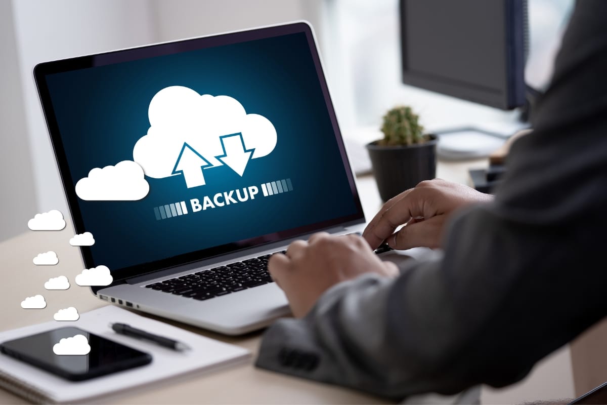 A person is using a laptop, showcasing the seamless efficiency of cloud backup services with a prominent icon on the screen.