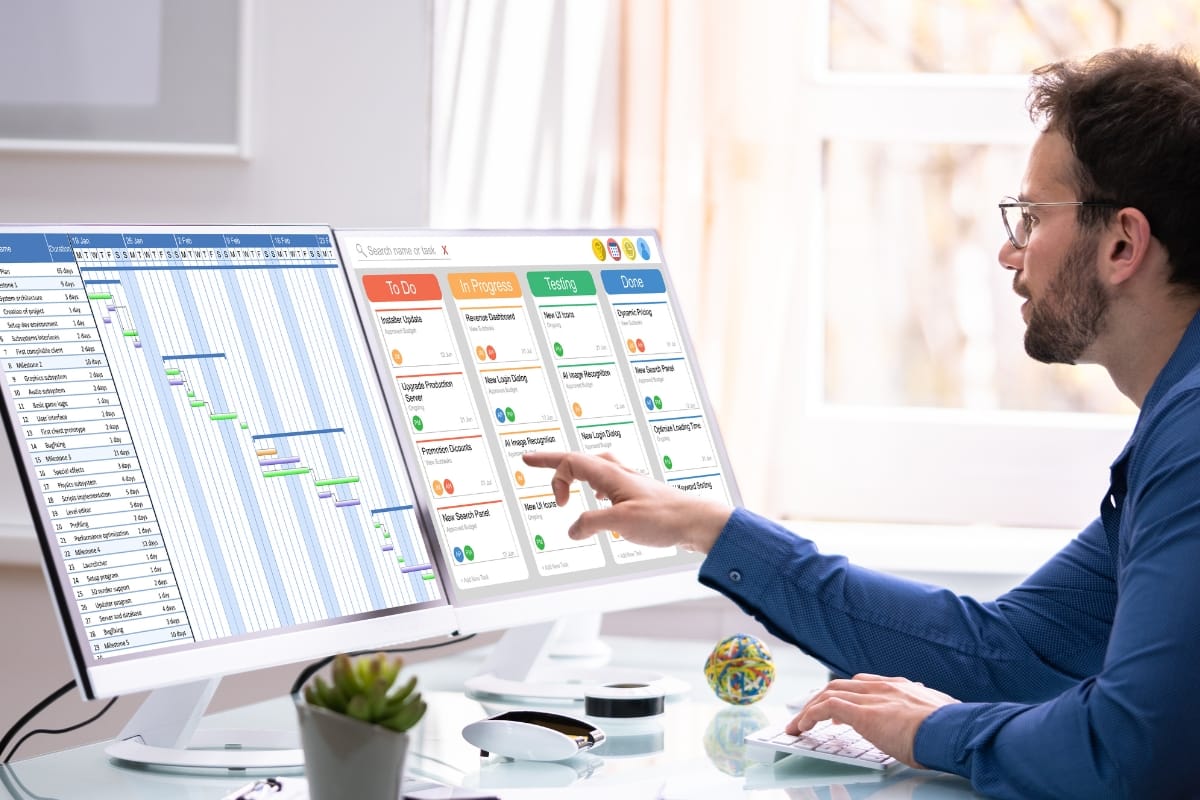 A person works at a desk with dual monitors displaying a Gantt chart and a task board, seamlessly integrating content calendar planning into their workflow.