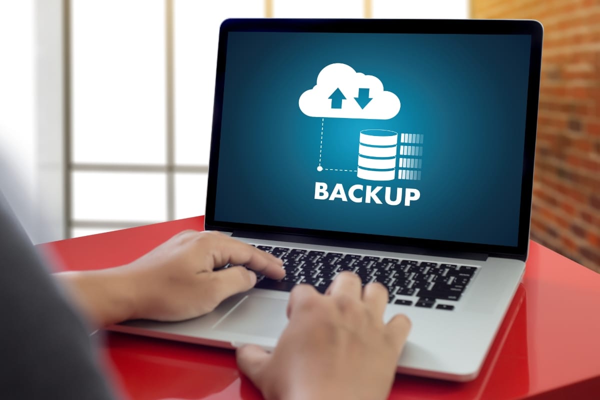 Hands typing on a laptop screen showing a cloud, arrows, and "BACKUP" text, symbolizing the seamless integration of database cleanup into the data backup process.