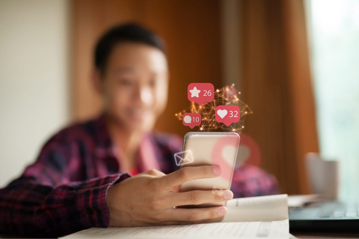 A person holds a smartphone displaying social media notifications, including likes and messages. The background is softly blurred, emphasizing the focus on engaging content creation showcased on the phone.